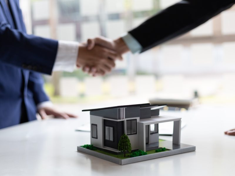 Businessman and real estate agent shaking hands after negotiating home purchase agreement.